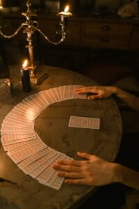 Mains disposant des cartes de tarot sur une table faiblement éclairée avec des bougies, créant une atmosphère mystérieuse.